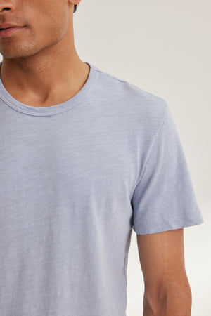 A model wears the SPADER TEE by Velvet by Graham & Spencer, a light gray, relaxed-fit short-sleeve top with a classic crew neck, shown from shoulders to mid-torso against a plain background.