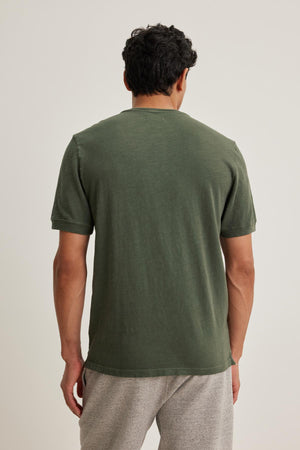 Someone wearing a green VITO HENLEY by Velvet by Graham & Spencer and gray pants stands with their back to the camera against a neutral background, showcasing a textured look.