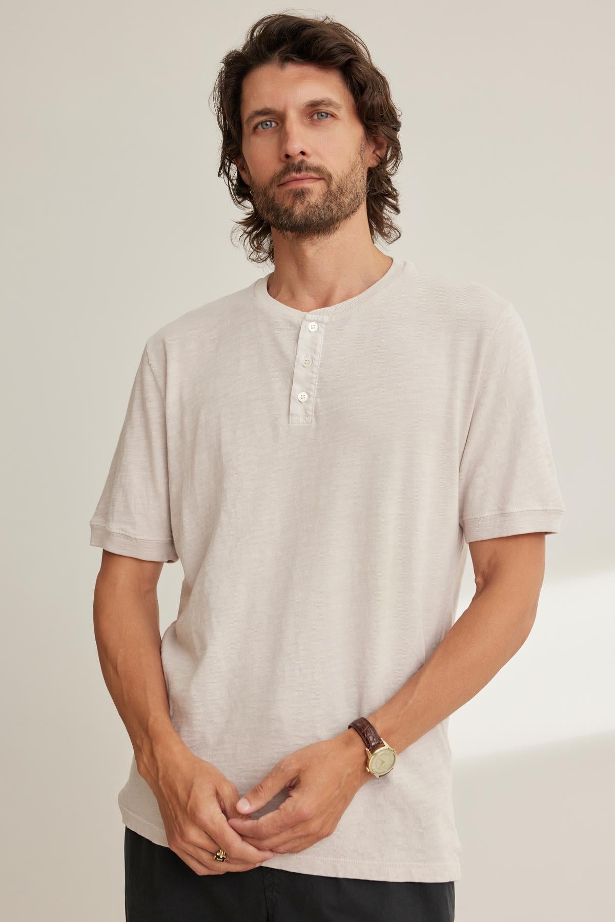 A man with long hair and a beard stands wearing the Velvet by Graham & Spencer VITO HENLEY, offering a textured feel. He wears a watch and gazes forward against a plain background.-38643365839041