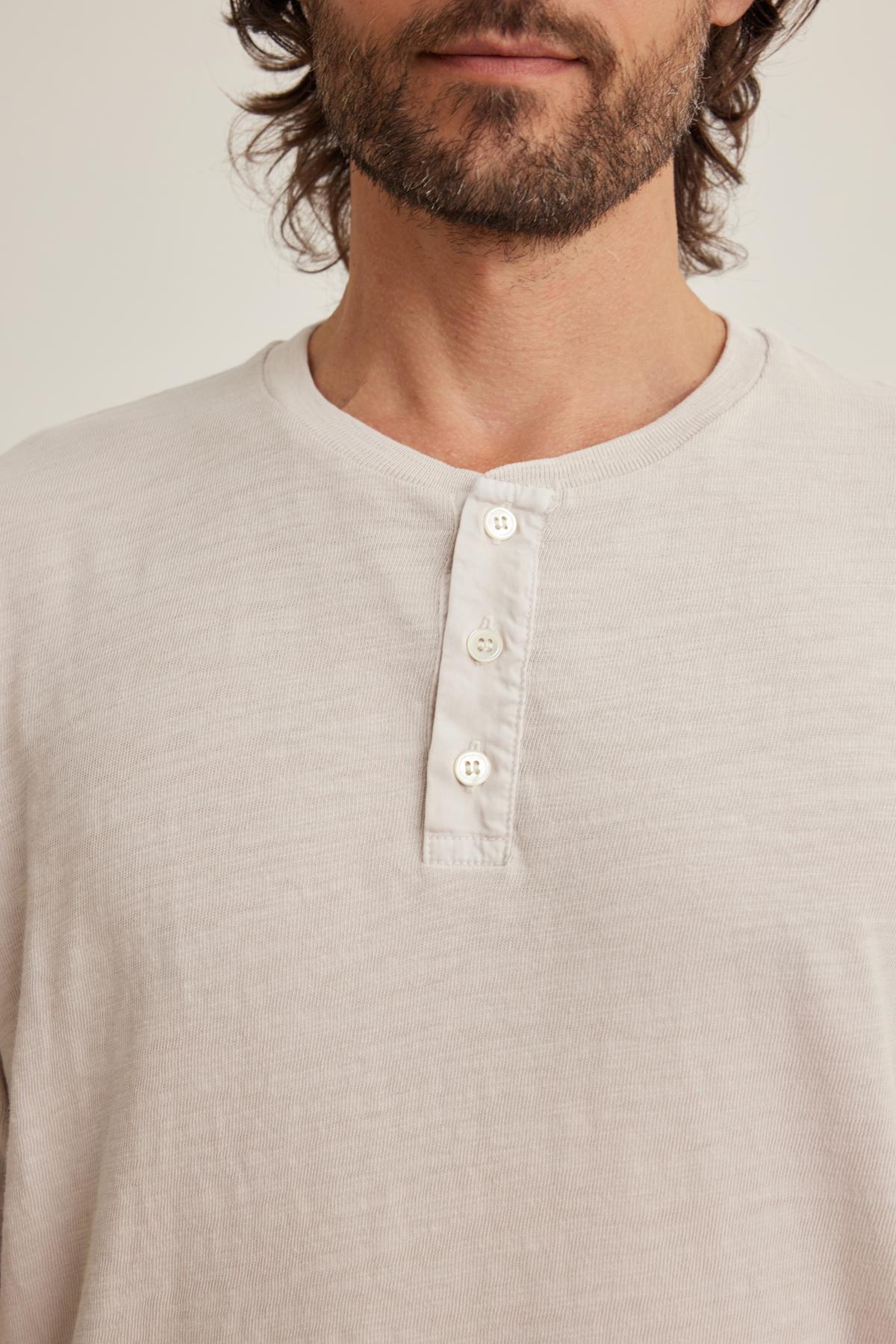 The image features a person wearing Velvet by Graham & Spencer's VITO HENLEY, a light-colored shirt crafted from soft Peruvian cotton, featuring a three-button placket and a textured feel, shown from shoulders to chest.-38643365707969