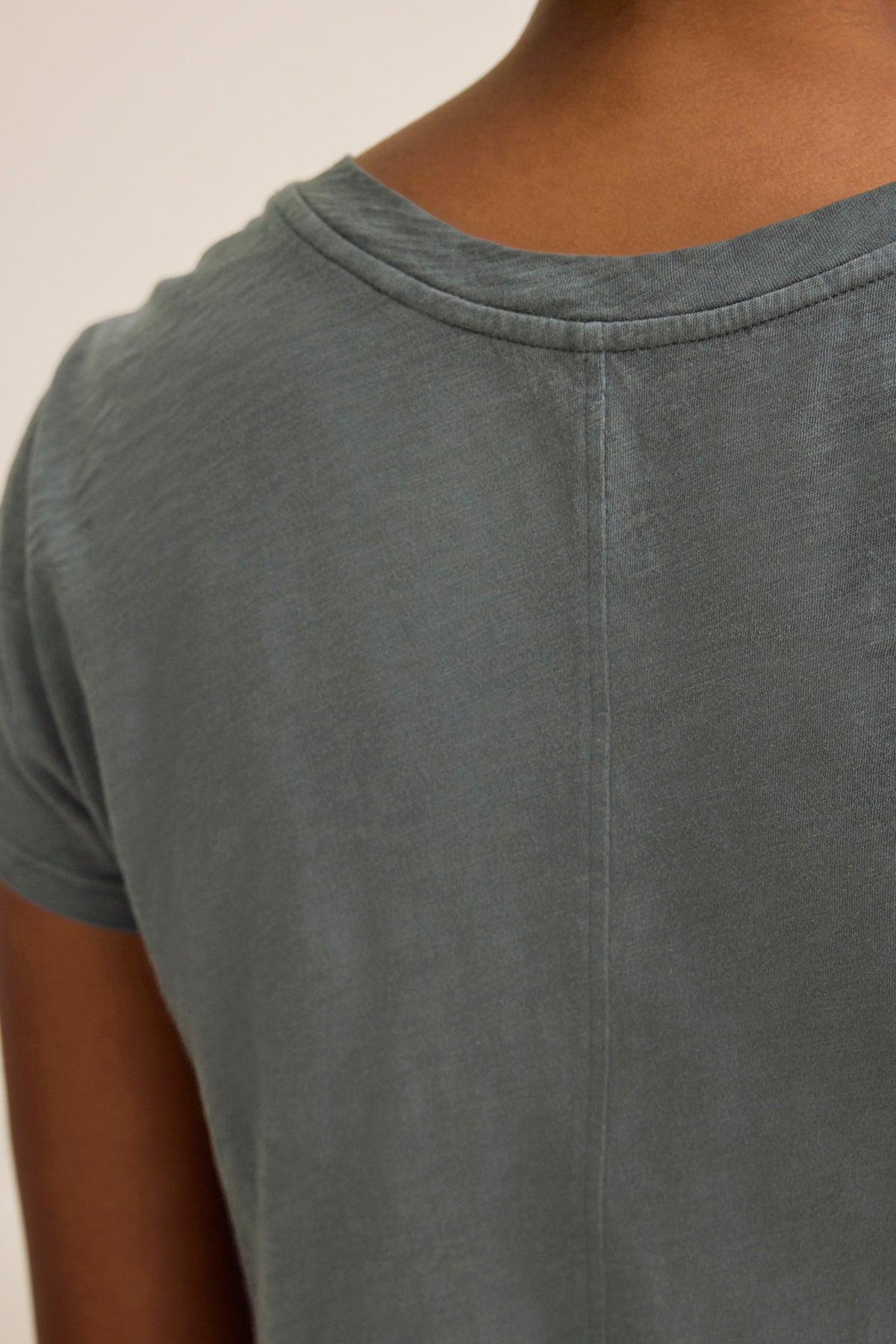 Close-up of a person wearing the ODELIA TEE by Velvet by Graham & Spencer, featuring faded green cotton slub fabric. The image highlights the upper back and shoulder seam, showcasing this versatile tee as a true wardrobe essential.-38928255090881
