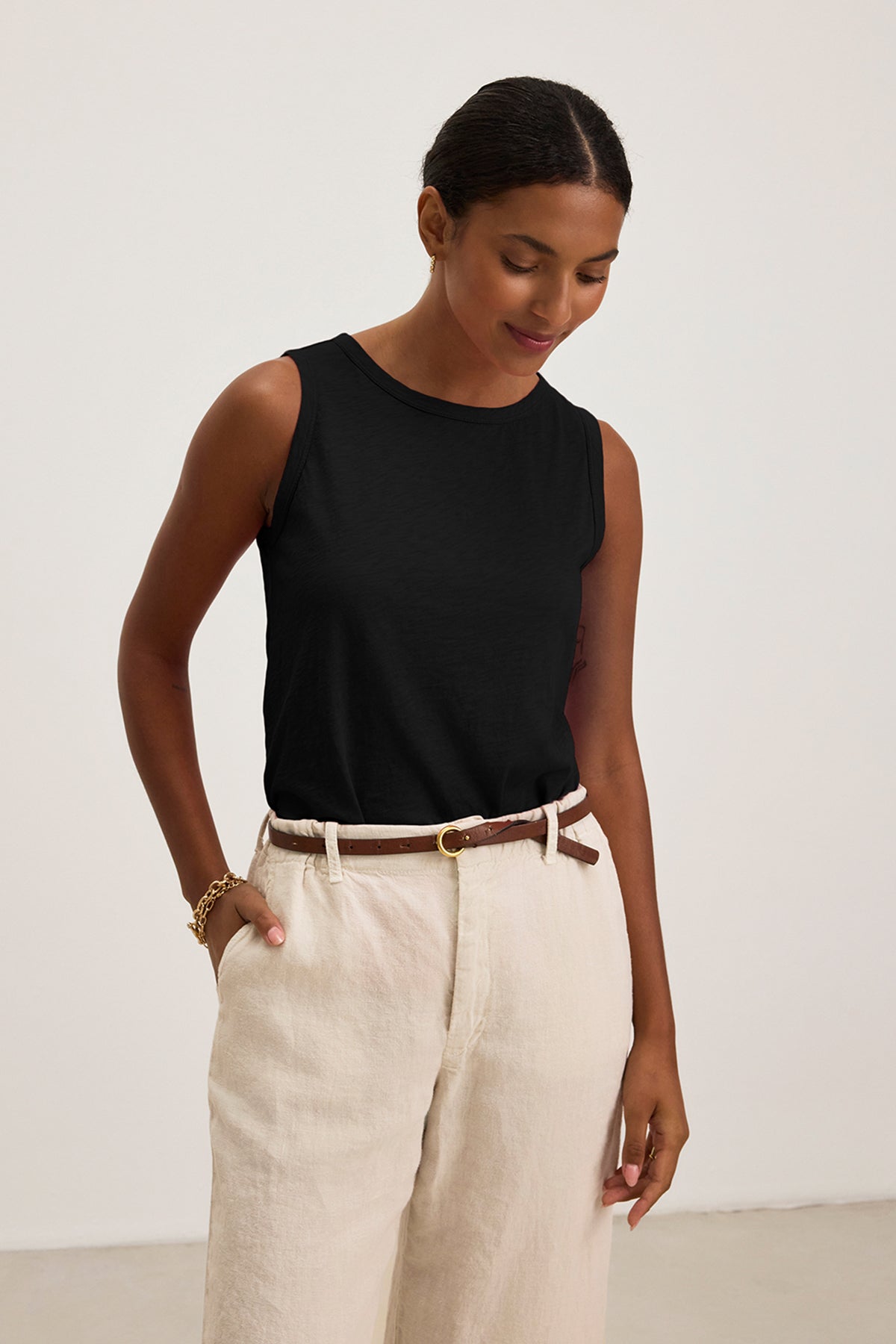 Wearing a Velvet by Graham & Spencer TAURUS TANK TOP and beige pants, a person with short dark hair stands against a plain light background, looking down with hands in pockets.-38865984061633