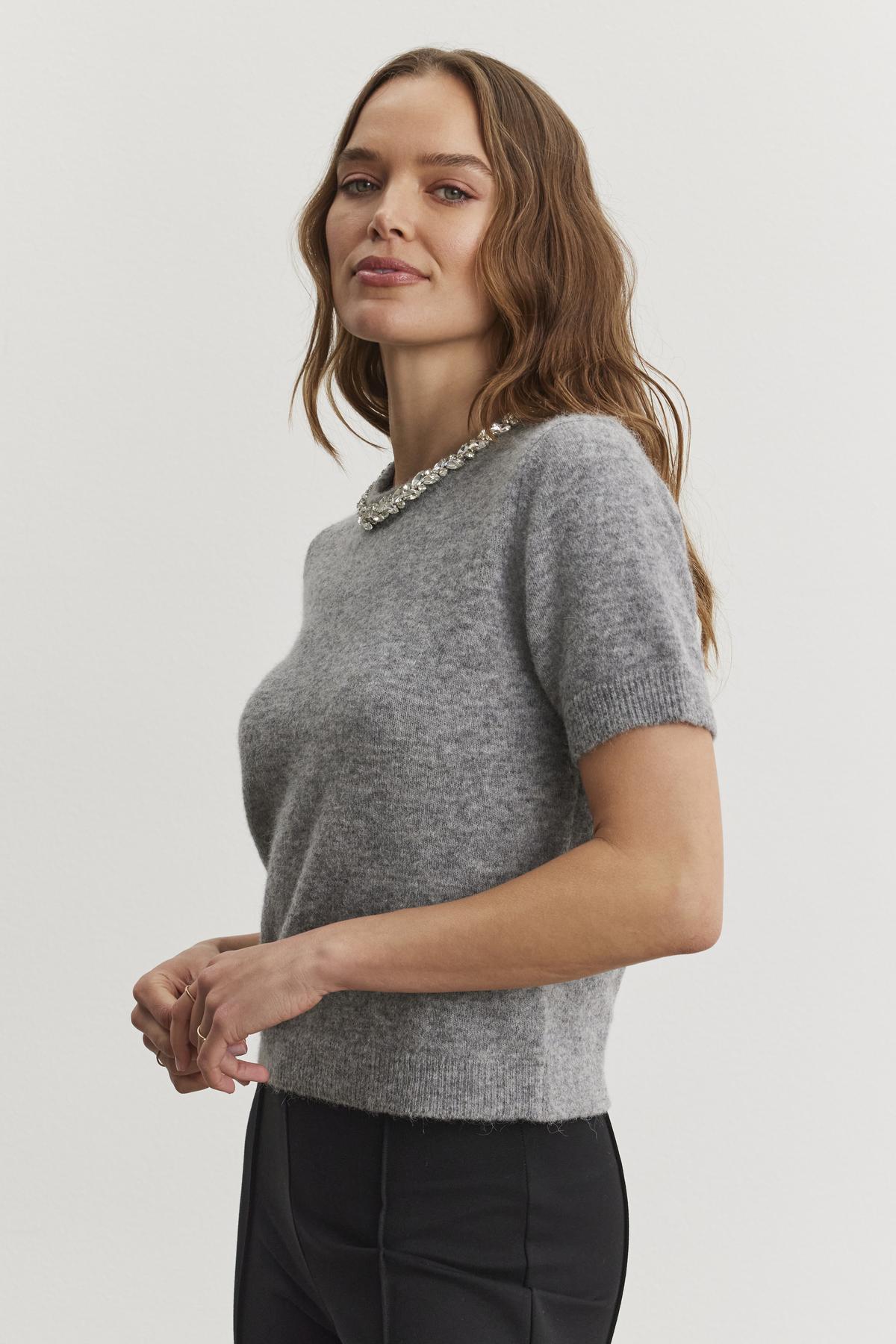 A woman with long hair wears the Velvet by Graham & Spencer LAYTON ALPACA EMBELLISHED SWEATER and black pants, standing against a plain background.