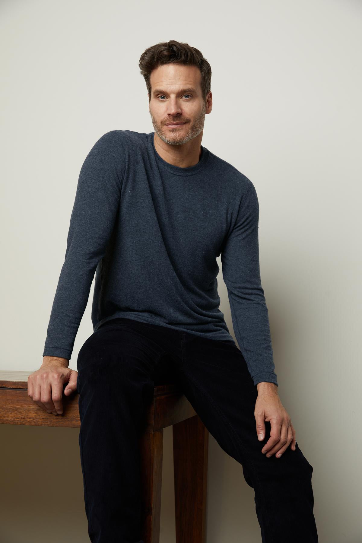 A man sitting on a Velvet by Graham & Spencer cozy wooden table wearing a Velvet by Graham & Spencer soft blue long sleeved shirt.-36320567984321