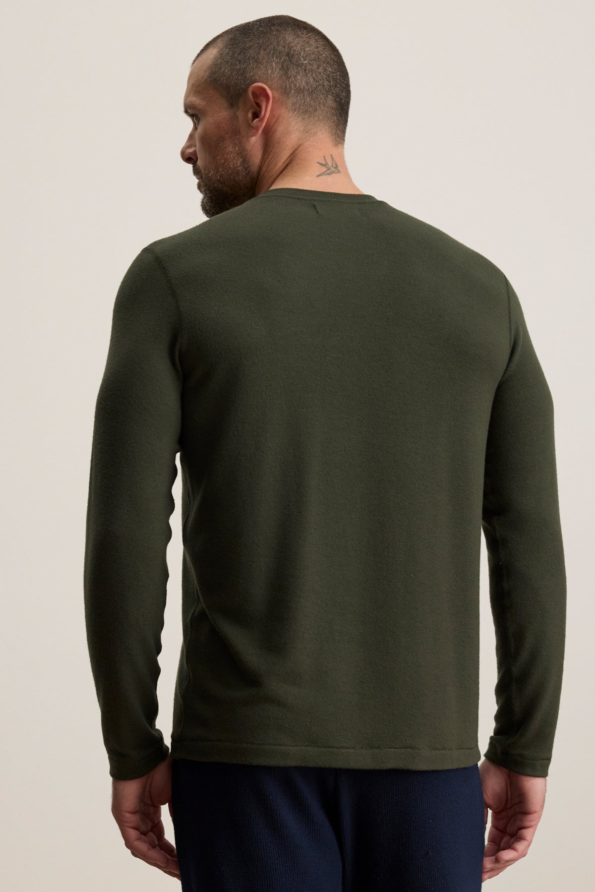 Man with short hair and a neck tattoo wearing the Velvet by Graham & Spencer BECKER CREW, a fitted long-sleeve dark green shirt, viewed from the back against a plain light background—ideal for everyday wear.