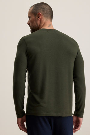 Man with short hair and a neck tattoo wearing the Velvet by Graham & Spencer BECKER CREW, a fitted long-sleeve dark green shirt, viewed from the back against a plain light background—ideal for everyday wear.