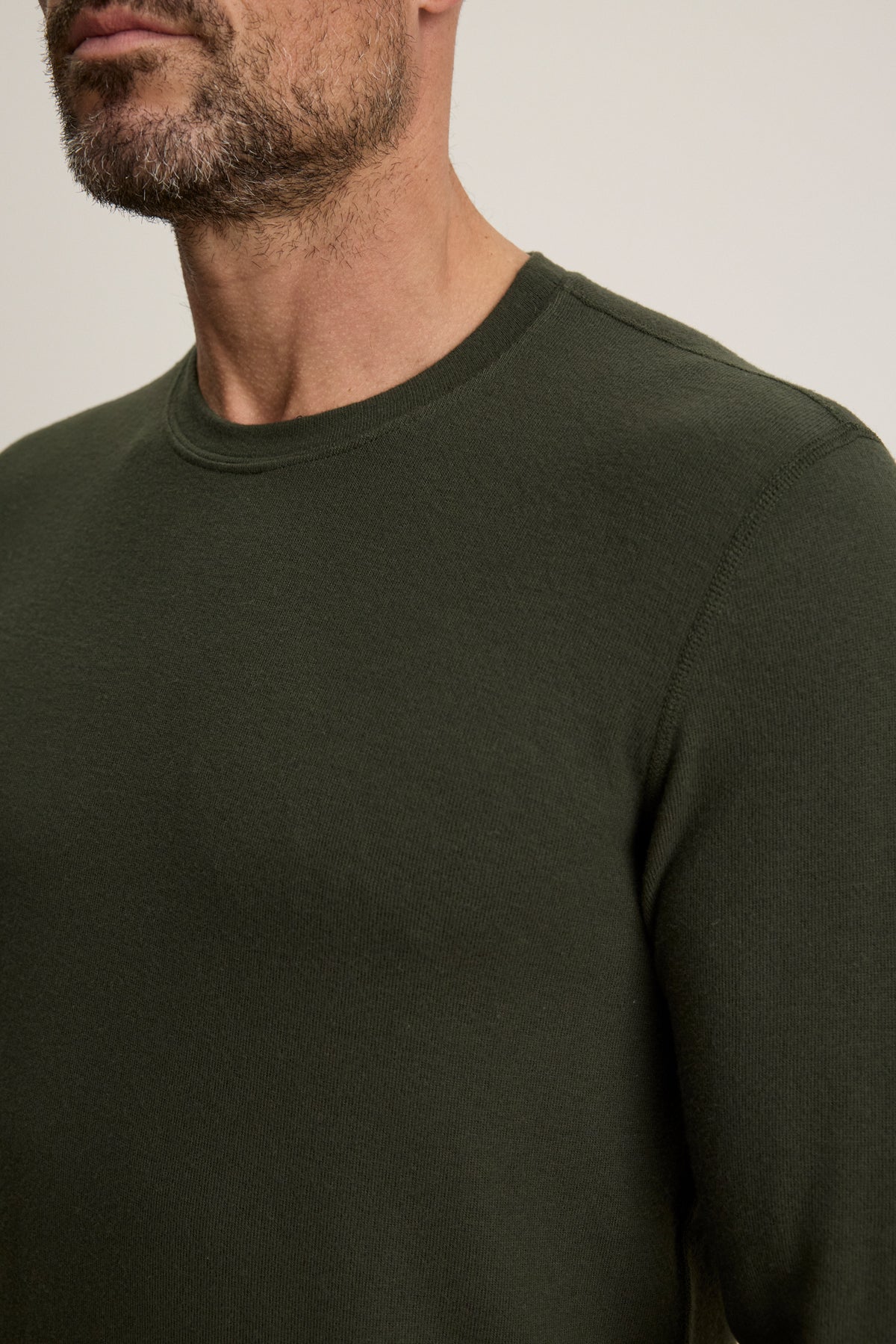 A man with a trimmed beard wears the Velvet by Graham & Spencer BECKER CREW, a fitted dark green sweater; the image shows his upper torso and part of his face.
