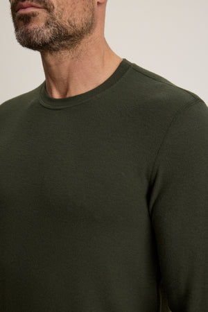 A man with a trimmed beard wears the Velvet by Graham & Spencer BECKER CREW, a fitted dark green sweater; the image shows his upper torso and part of his face.