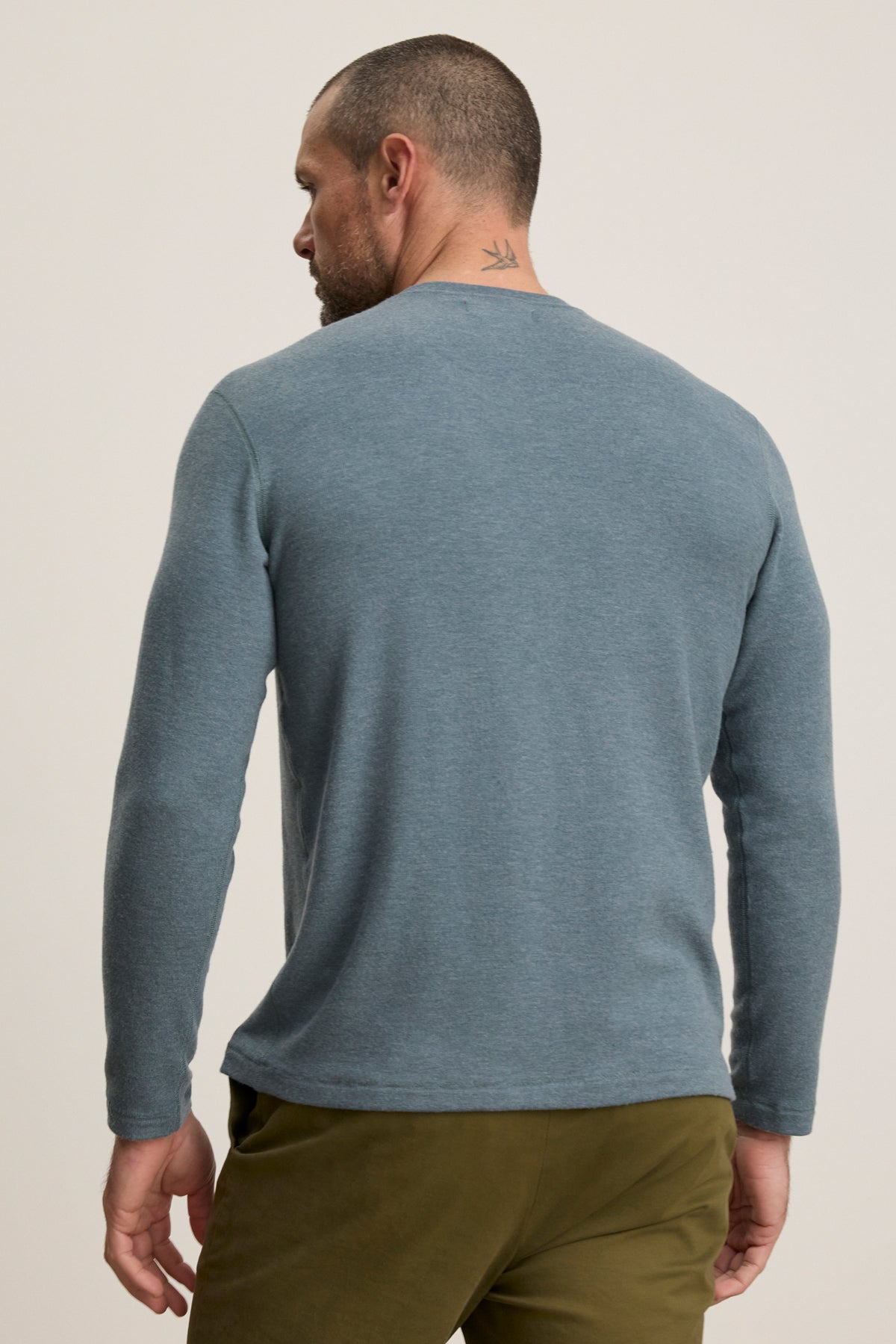 Man wears the BECKER CREW by Velvet by Graham & Spencer—a fitted light blue long-sleeve crew neck shirt with olive green pants, shown from the back against a plain background. Ideal for everyday style.