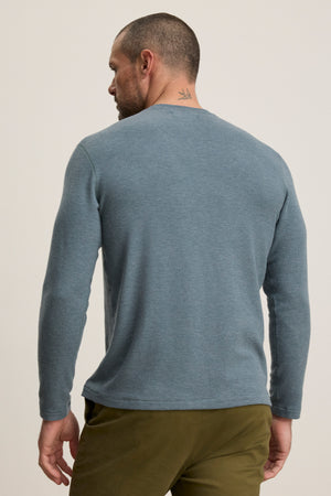 Man wears the BECKER CREW by Velvet by Graham & Spencer—a fitted light blue long-sleeve crew neck shirt with olive green pants, shown from the back against a plain background. Ideal for everyday style.