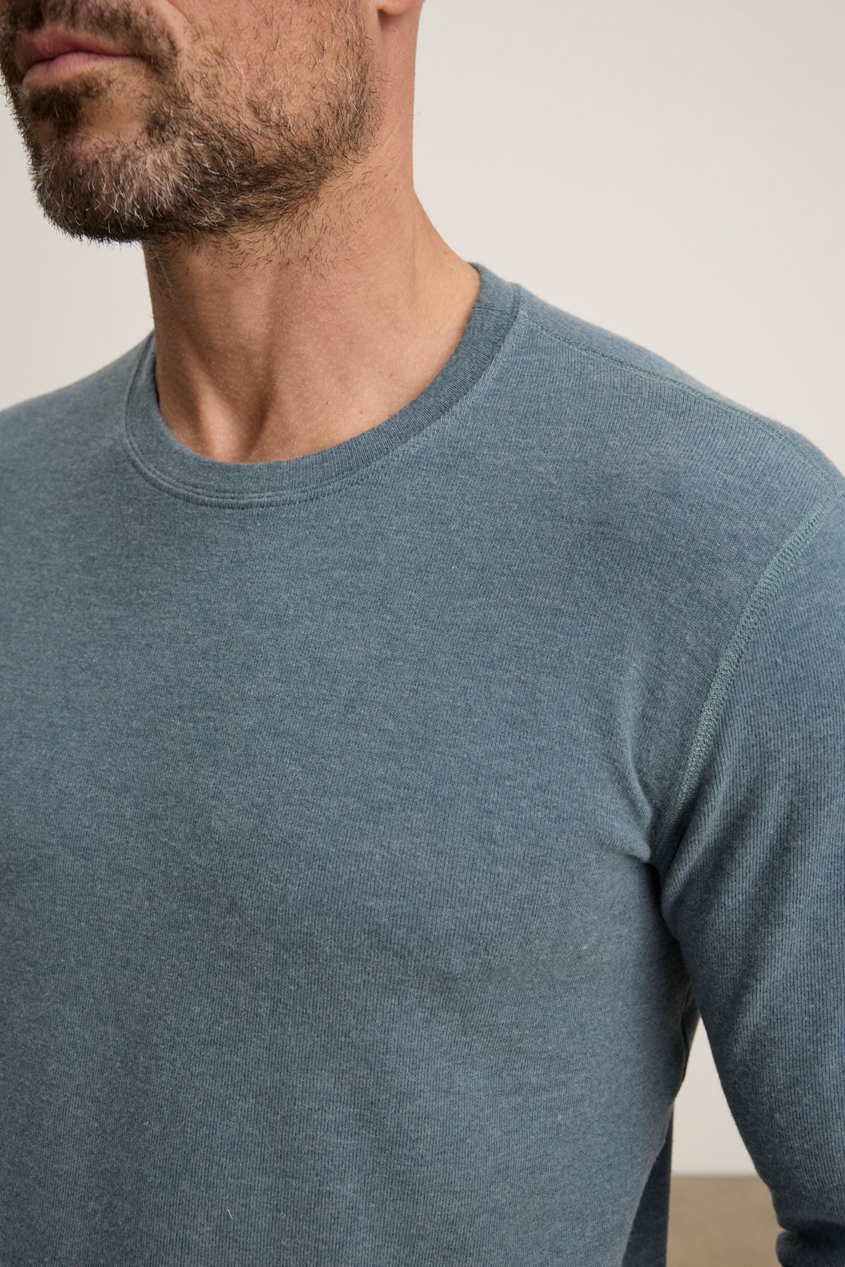 A man with a trimmed beard is shown from the shoulders up wearing the Velvet by Graham & Spencer BECKER CREW, a fitted light blue, long-sleeve jersey shirt.