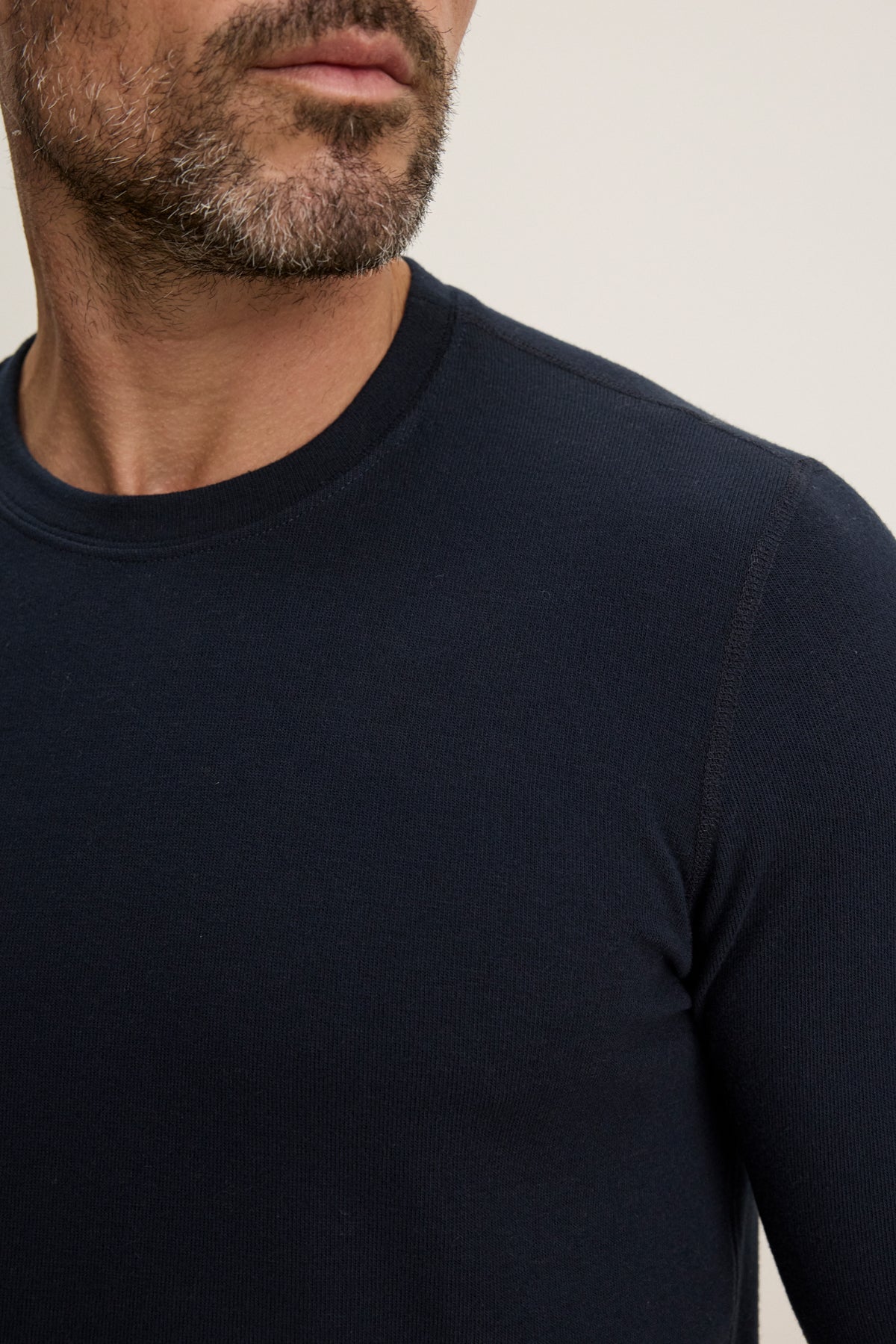 A close-up of a man wearing the BECKER CREW, a navy blue long-sleeve fitted crew neck shirt by Velvet by Graham & Spencer, showing part of his face and torso.
