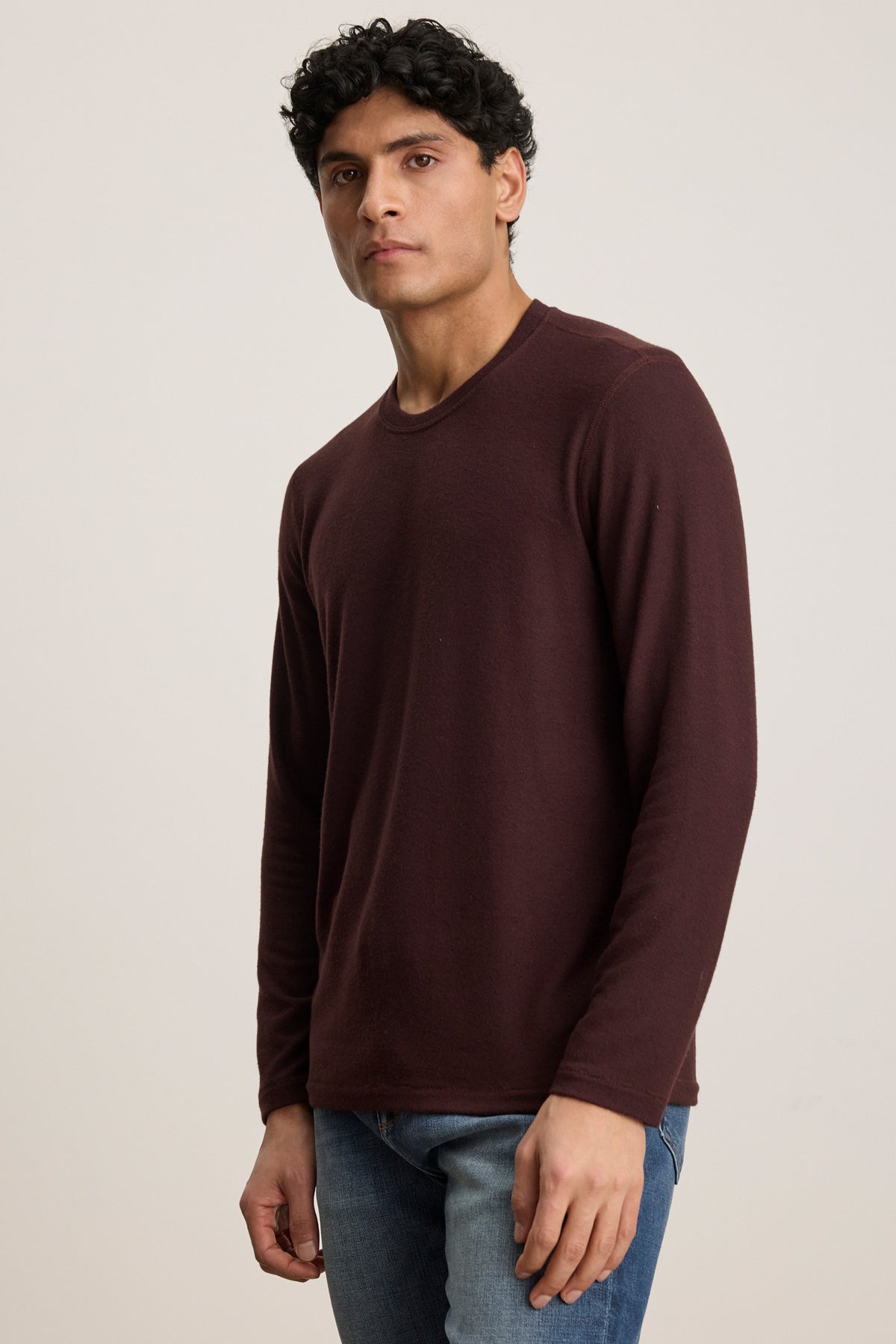 A man wearing the BECKER CREW sweater in burgundy by Velvet by Graham & Spencer and blue jeans stands against a plain light background, looking at the camera.