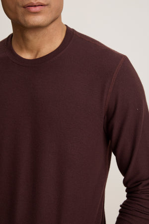 A person is shown from shoulders to mid-torso against a neutral background wearing the BECKER CREW, a plain, long-sleeve, dark maroon fitted crew neck shirt by Velvet by Graham & Spencer.
