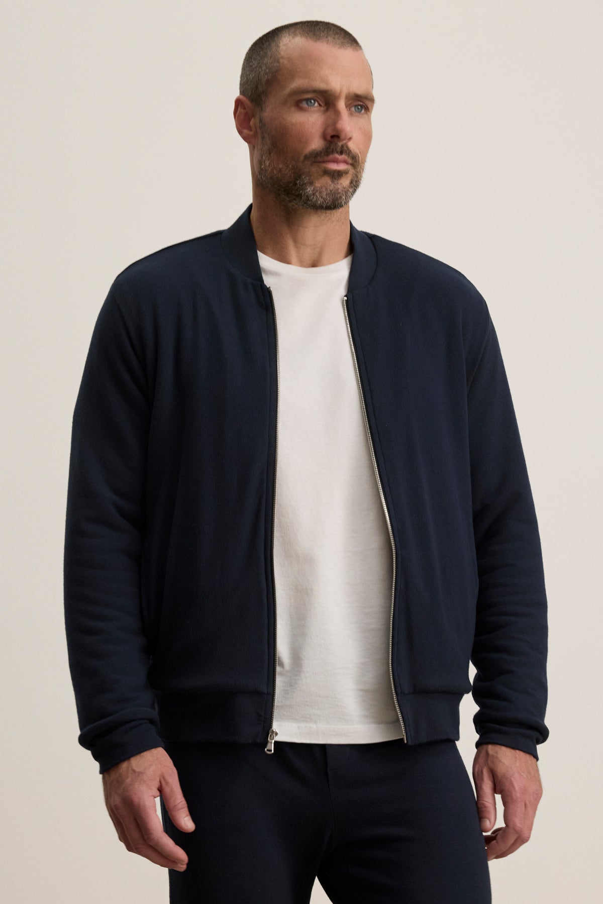 A man wearing the Velvet by Graham & Spencer MILES JACKET in navy over a white t-shirt and navy pants stands against a plain light background.