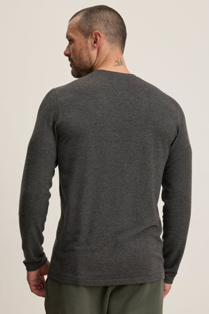 A man with short hair and a neck tattoo wears Velvet by Graham & Spencer’s RYLAND HENLEY, a cozy long-sleeve dark gray 3-button jersey, and green pants, shown from the back—ideal for casual occasions.