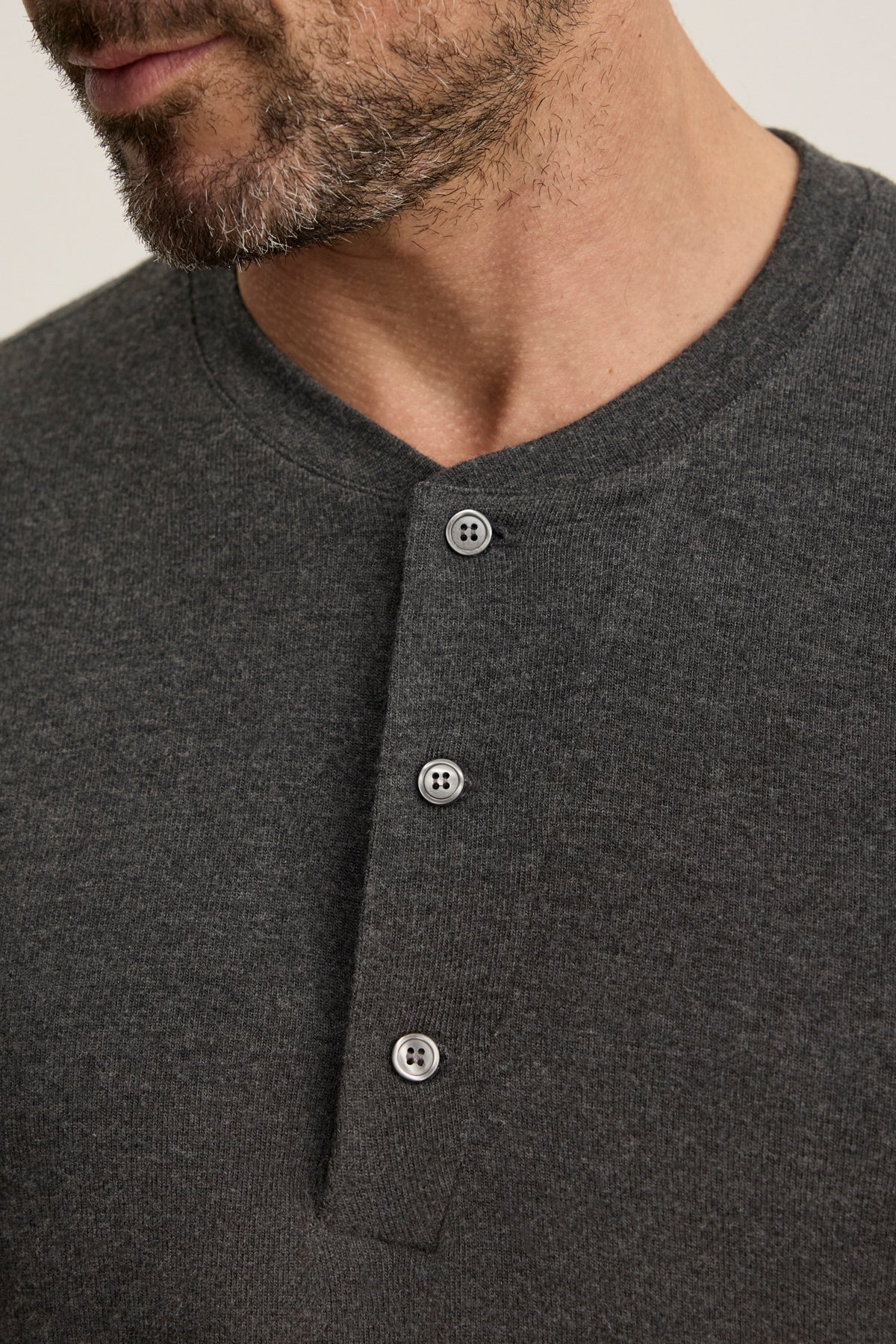 Close-up of a man wearing the RYLAND HENLEY from Velvet by Graham & Spencer, a dark gray, textured 3-button jersey shirt perfect for casual occasions.