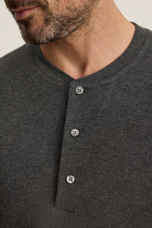 Close-up of a man wearing the RYLAND HENLEY from Velvet by Graham & Spencer, a dark gray, textured 3-button jersey shirt perfect for casual occasions.