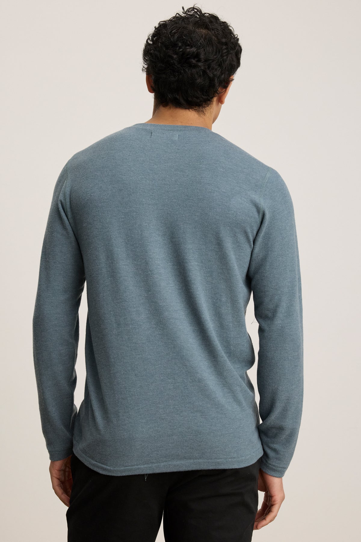 A person faces away from the camera, wearing the Velvet by Graham & Spencer RYLAND HENLEY long-sleeve jersey in blue and black pants, set against a plain light background.