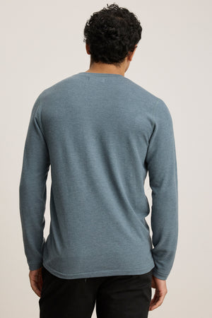A person faces away from the camera, wearing the Velvet by Graham & Spencer RYLAND HENLEY long-sleeve jersey in blue and black pants, set against a plain light background.
