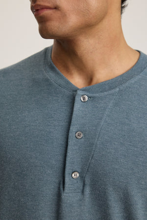 A person wearing the RYLAND HENLEY by Velvet by Graham & Spencer— a blue, three-button jersey shirt— is shown from the shoulders to just above the mouth.