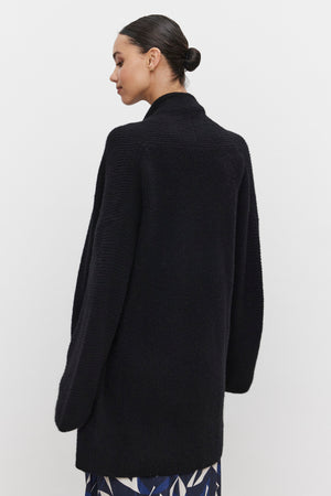 A person with their hair in a bun is wearing the CALLI CARDIGAN by Velvet by Graham & Spencer and a patterned skirt, viewed from behind against a white background.