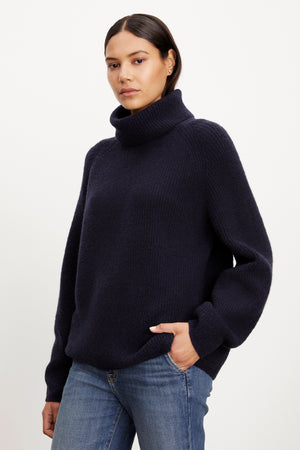 A model wearing a cozy Velvet by Graham & Spencer JUDITH turtleneck sweater and jeans.