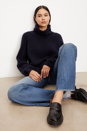 The model is sitting on the floor wearing a Velvet by Graham & Spencer JUDITH TURTLENECK SWEATER.