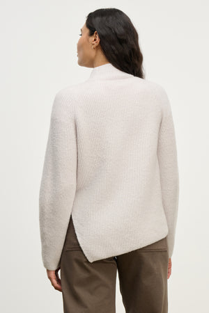 A woman is shown from behind wearing the LESA SWEATER by Velvet by Graham & Spencer, a light-colored, ribbed mock neck style, paired with brown pants against a plain background.