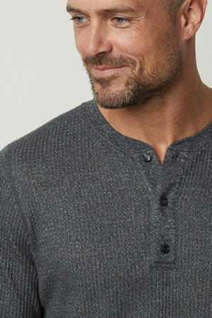 A man wearing a Velvet by Graham & Spencer Anthony Thermal Henley sweater with a waffle texture.
