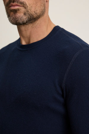 Close-up of a man wearing the TOBIAS CREW by Velvet by Graham & Spencer—a dark blue, long-sleeve sweater made from cozy thermal fabric. Only his lower face, neck, and upper torso are visible.