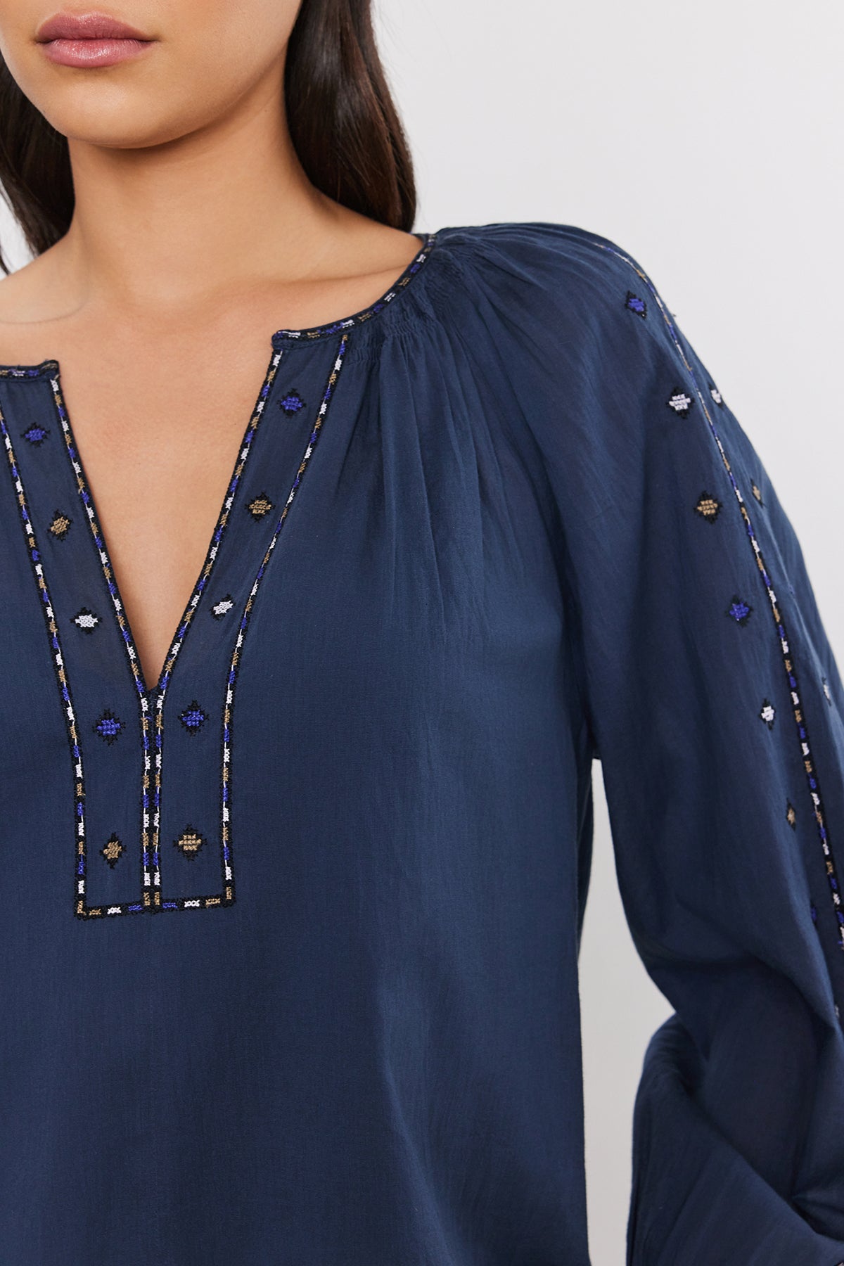 A person wearing a dark blue TINA TOP by Velvet by Graham & Spencer with a V-neckline and long puff sleeves. Only the torso and lower part of the face are visible.-37452699730113