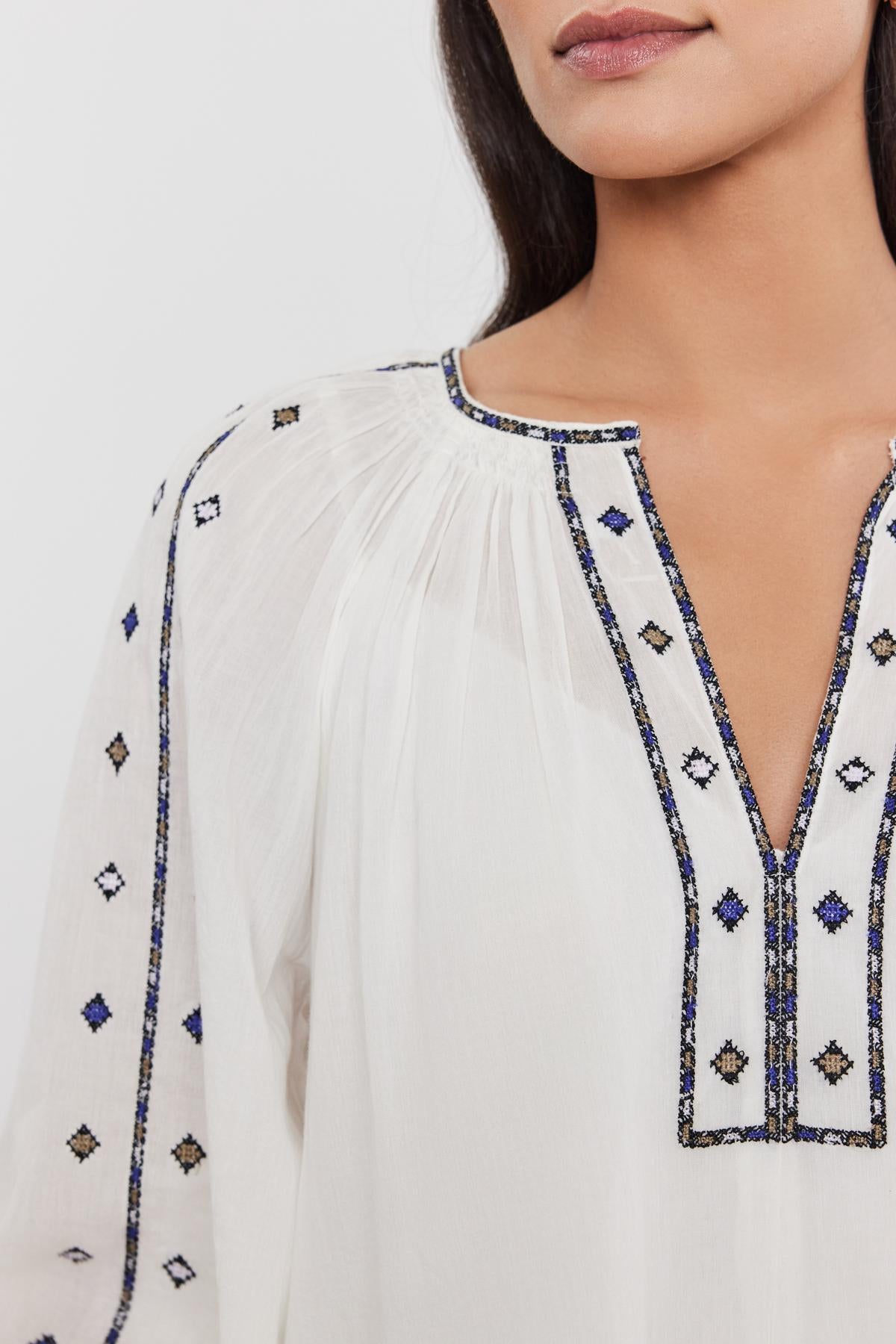 Close-up of a woman wearing a Velvet by Graham & Spencer Tina Top with a detailed neckline embroidered with blue and black geometric designs.-36752975593665