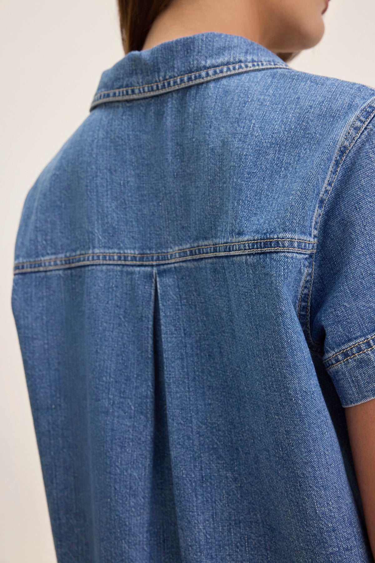 A close-up of someone wearing the DELANA DENIM DRESS by Velvet by Graham & Spencer, highlighting the back and shoulder seam details.-38802060148929