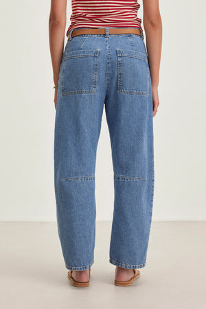 Someone wearing a red and white striped top, Velvet by Graham & Spencer's FARAH DENIM PANT with large back pockets, a brown belt, and sandals, standing on a light surface.