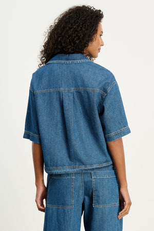 A person with curly hair models the KADDY DENIM TOP by Velvet by Graham & Spencer and matching relaxed-fit denim pants, shown from the back against a plain light background.