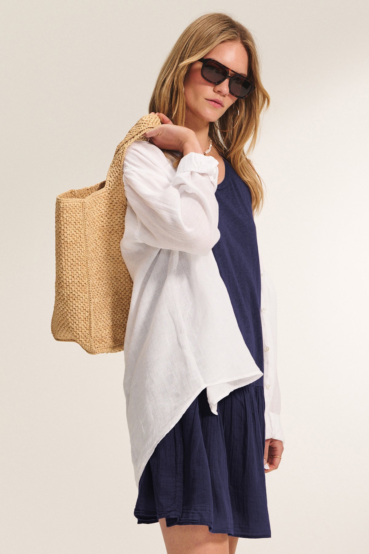 A woman wearing the DENNA DRESS by Velvet by Graham & Spencer, paired with sunglasses, a white cotton slub top, and a woven straw tote bag, stands against a plain background.-39292877308097
