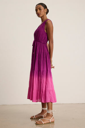 A woman stands sideways against a plain background wearing the Velvet by Graham & Spencer MARILYN DRESS—a sleeveless, dip-dye crinkle voile midi dress with a belted waist—and white strappy flat sandals.