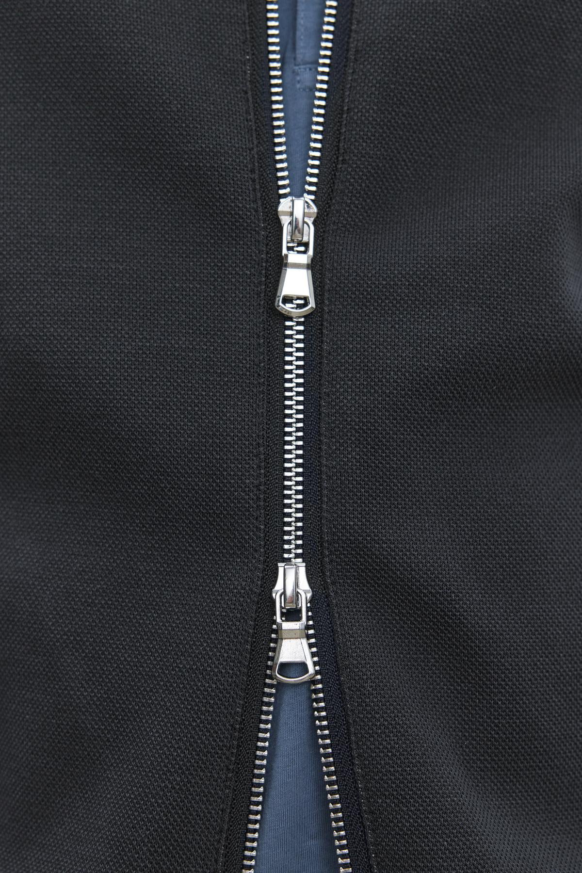 Close-up of the partially opened double zipper on the RYDELL JACKET by Velvet by Graham & Spencer, highlighting the metal teeth and two slider pull tabs against the black textured cotton blend fabric.