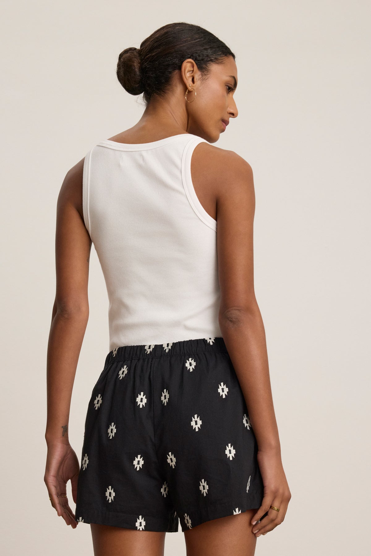 A woman with her hair in a bun is seen from behind wearing a white sleeveless top and Velvet by Graham & Spencer's DAPHNE EMBROIDERED COTTON VOILE SHORT featuring black cotton and white embroidery.