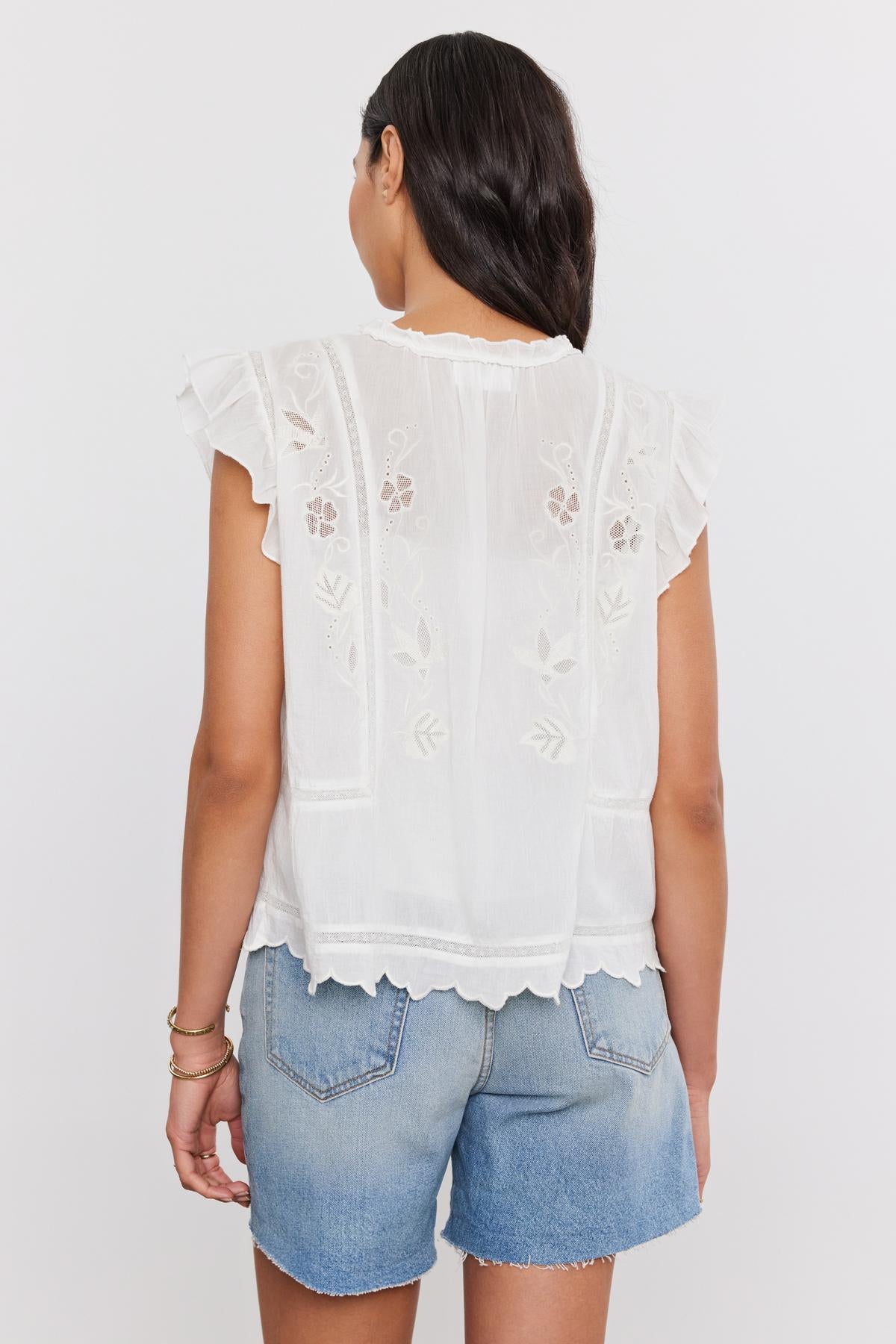 A woman viewed from behind wearing a CHARLENE TOP by Velvet by Graham & Spencer with cotton embroidery and blue denim shorts.-36830326816961