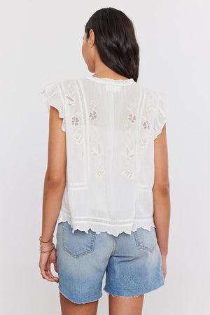 A woman viewed from behind wearing a CHARLENE TOP by Velvet by Graham & Spencer with cotton embroidery and blue denim shorts.