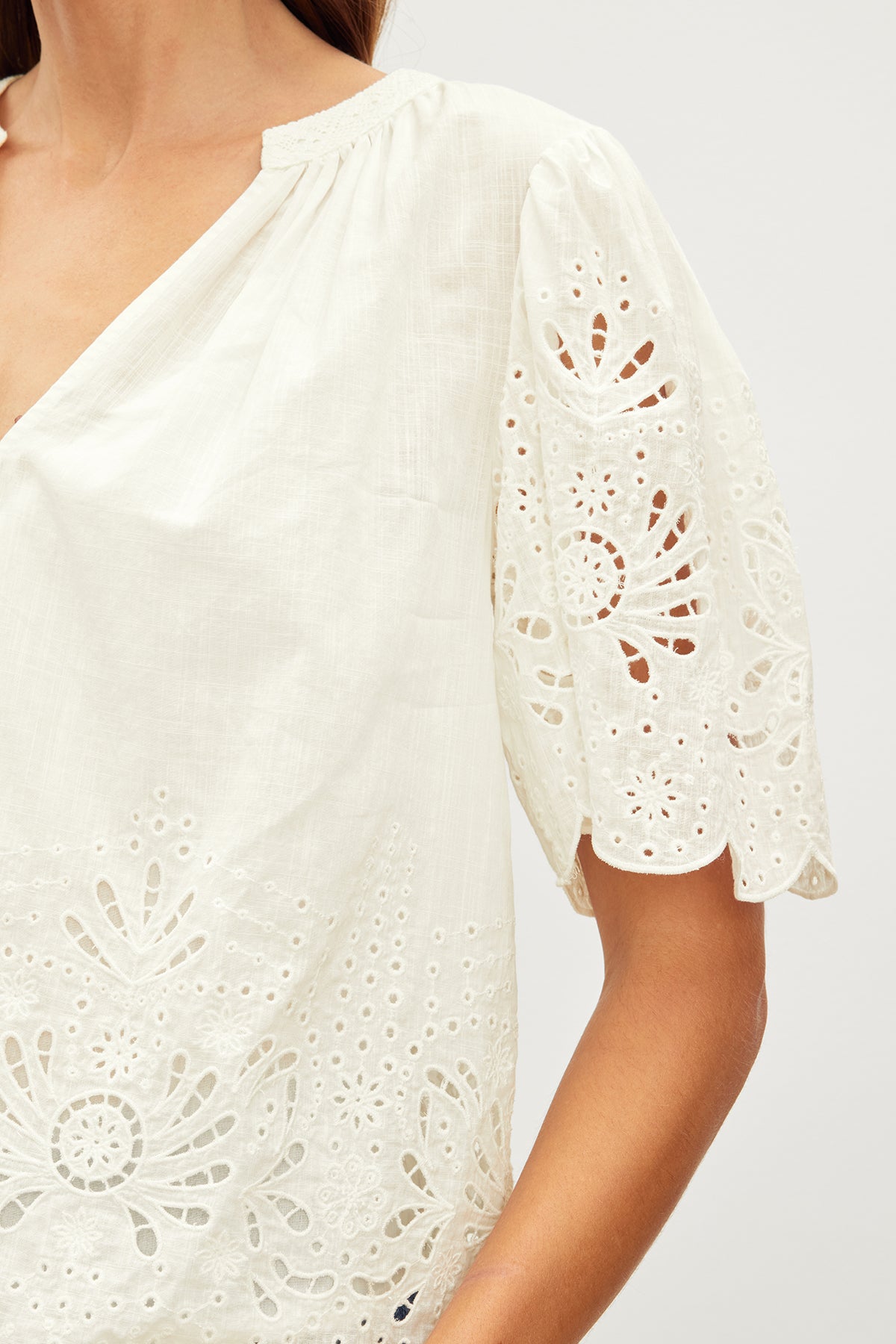   Close-up of a woman's shoulder and arm wearing a Velvet by Graham & Spencer Razi Embroidered Cotton Lace Top with cut-out patterns on the sleeve. 