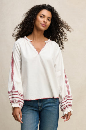 A woman with curly hair wears the SCARLETT TOP by Velvet by Graham & Spencer, a white puff sleeve top, with blue jeans.