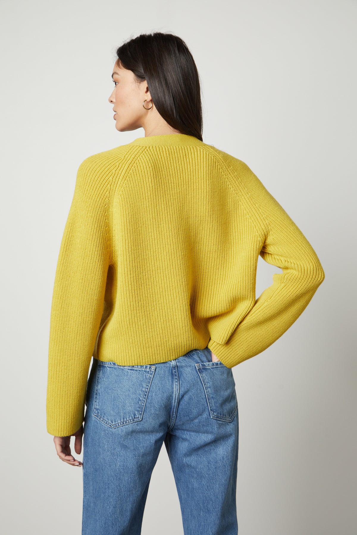 The back view of a woman wearing a Velvet by Graham & Spencer MARILYN BUTTON FRONT CARDIGAN in sunflower yellow and jeans.-26727746994369