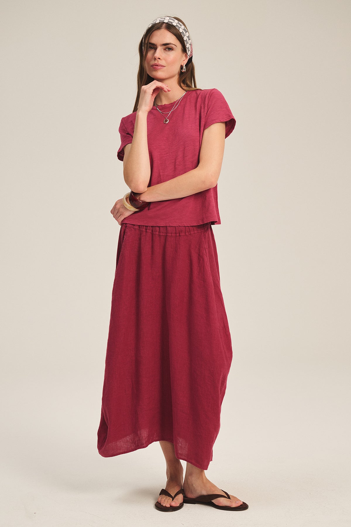 A woman stands against a plain background wearing the Velvet by Graham & Spencer MARIE TEE in dark pink cotton slub with a matching long skirt, black sandals, and a patterned headband.