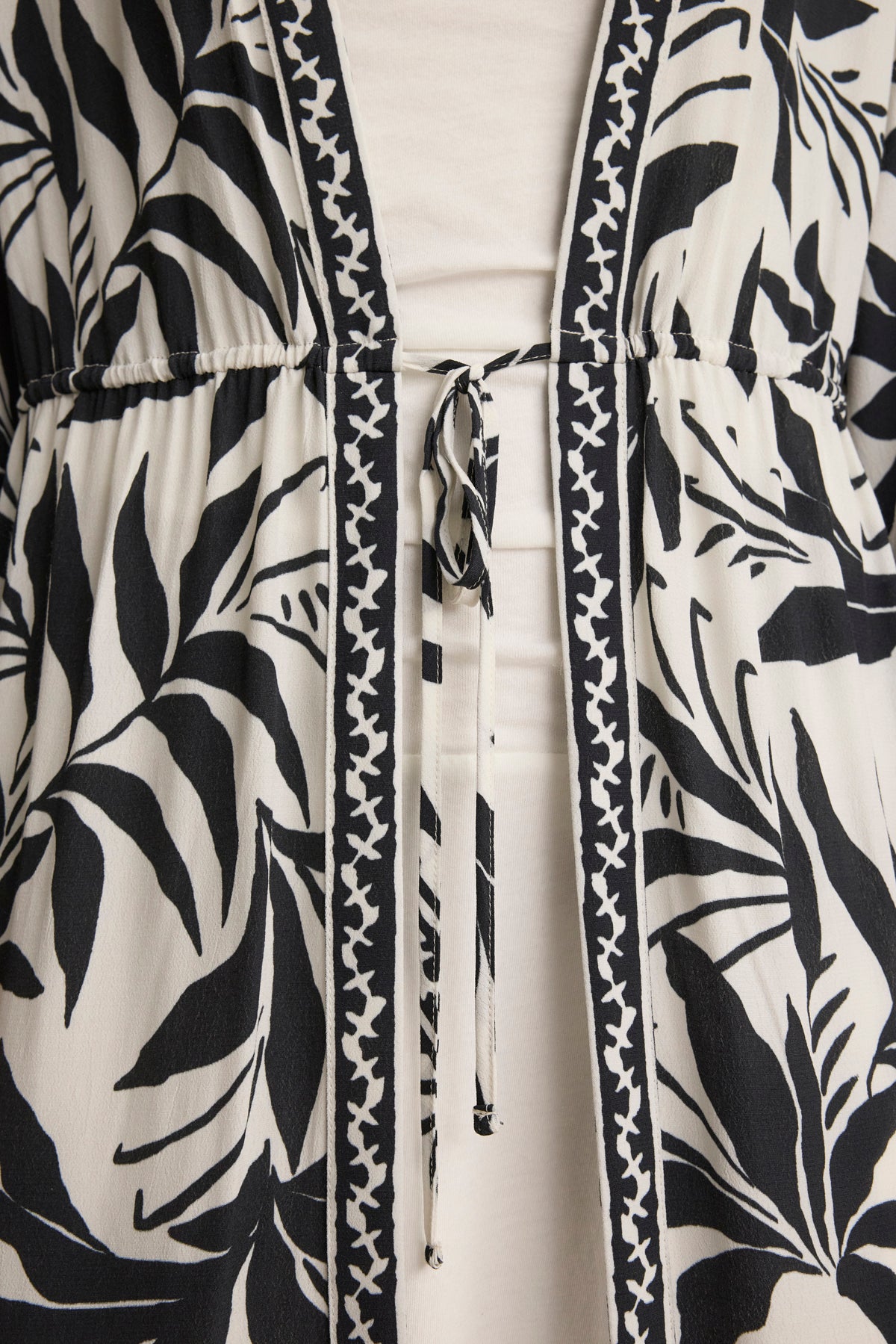 Close-up of the ADDISON COVER UP DRESS by Velvet by Graham & Spencer, showcasing black and white leaf patterns, an adjustable waist tie, and zigzag edge trim—a versatile caftan dress perfect as a cover-up for any occasion.