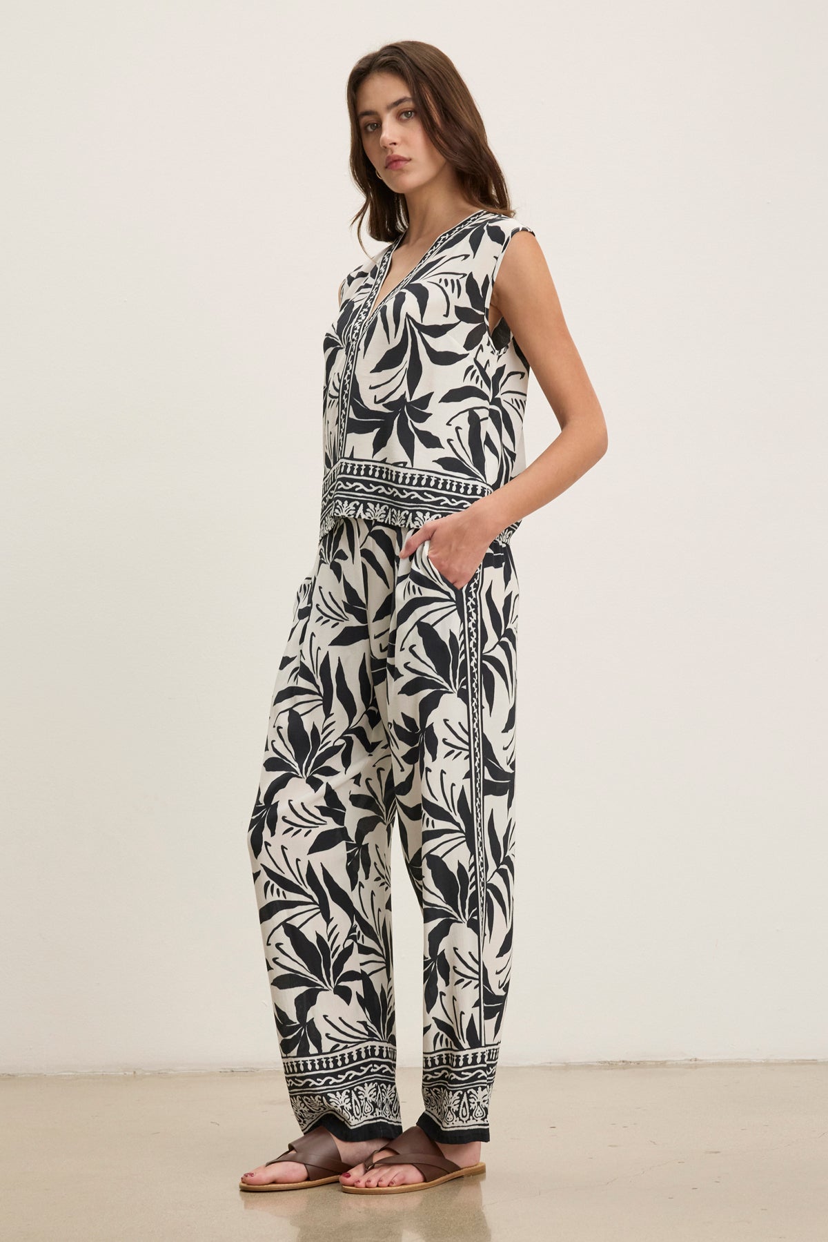 A woman stands against a plain background wearing the CLAUDIA PANT by Velvet by Graham & Spencer, a lightweight black and white printed viscose pant with pockets—ideal for beach days or as a vacation cover-up.-39145479536833