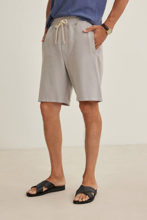 Wearing Velvet by Graham & Spencer's BOSLOW SHORT in relaxed fit light gray, paired with a blue shirt and black sandals, this look is the perfect warm-weather staple for effortless style.