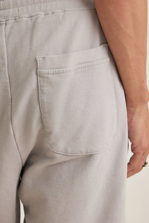 Close-up of the back pocket and waistband of the BOSLOW SHORT by Velvet by Graham & Spencer in light gray, with a person’s right arm partially visible—a true warm-weather staple.